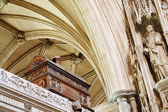 Photo inside Winchester Cathedral looking up towards the arches. Just underneath an arch, there is a dark brown inscribed box.
